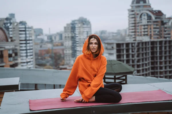 Chica con una chaqueta naranja posa en el techo de un edificio en el centro de la ciudad —  Fotos de Stock