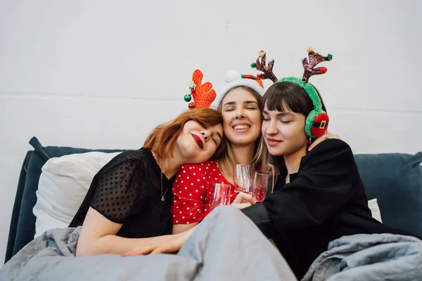 Sorrindo modelos femininos segurando copos de vinho e desfrutando de festa de pijama . — Fotografia de Stock