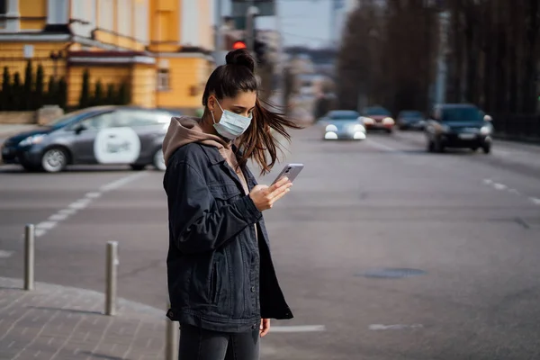 Menina em máscara protetora usando smartphone ao ar livre. COVID 19. pandemia de coronavírus mundial . — Fotografia de Stock