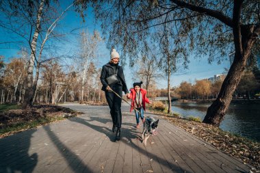 Mutlu anne ve kızı güz parkında köpekle yürüyor.