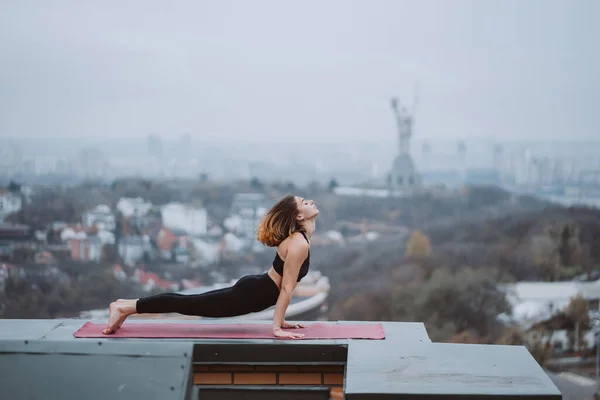 Donna che pratica yoga sul tappeto sul tetto e facendo esercizi di yoga — Foto Stock