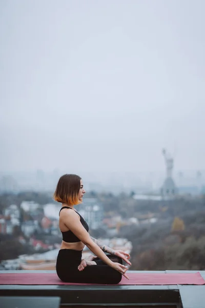 Woman practicing yoga on the mat on the roof and doing yoga exercises — Stock Photo, Image