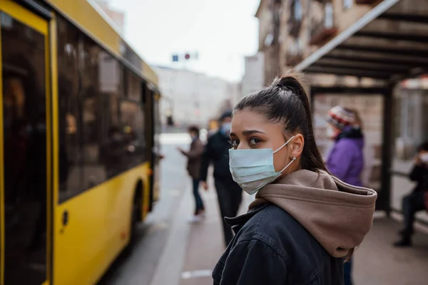Молодая женщина в хирургической маске на улице на автобусной остановке — стоковое фото