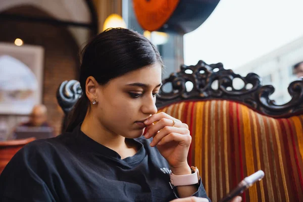 Pretty young girl resting on a big soft chair in a cafe, chatting on the phone — Stock Photo, Image