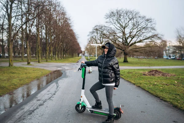 Mujer con chaqueta en un scooter eléctrico en un parque de otoño. — Foto de Stock
