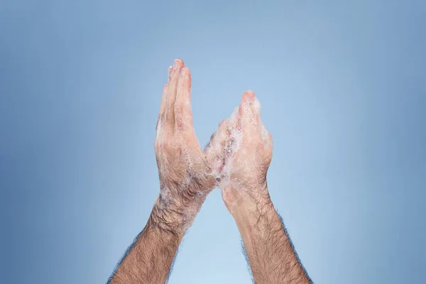 Hand washing with soap suds to achieve good prevention and hygiene. Mature man's hands with hairy arms. Close-up hands and smooth blue background.