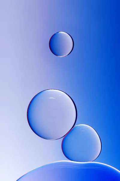 Macro photography of small drops of oil floating on water with blue background. Abstract composition of great beauty. Background for design.