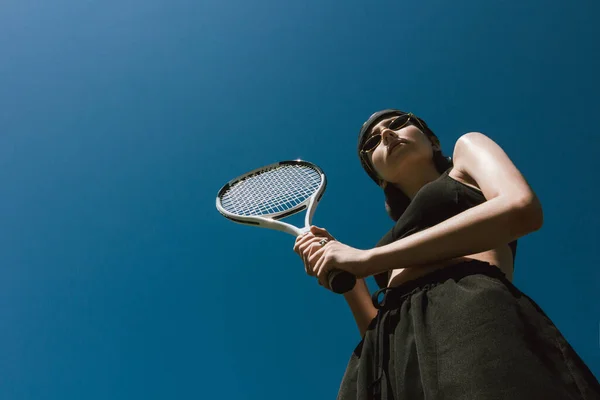 Girl on a tennis court Bottom view photo Girl in black sportswear is holding a tennis racket on blue sky background Photo with copy space