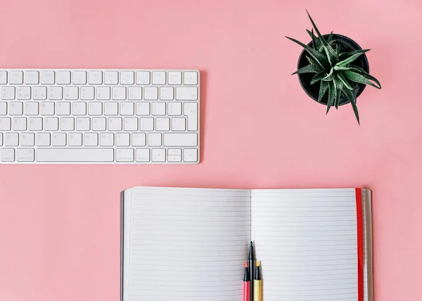 Office desk Top view photo with copy space Notebook with marker, keyboard and evergreen plant on pink background