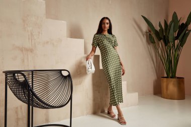 Moda mankeni esmer saçlar yeşil noktalar, ipek elbiseler, yüksek topuklar, aksesuarlar, partiler, yaz gezileri, çiçek saksısı, duvar merdivenleri, bronz tenli güzel kadın..