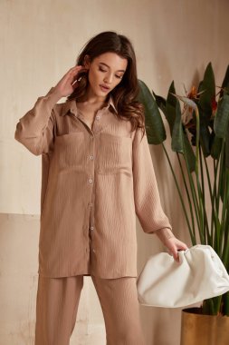 Güzel esmer kadın doğal makyaj kıyafetleri giyer günlük kıyafet ofis tarzı kıyafet giyer tamamen bej bluz ve pantolon takım elbise, romantik randevu işi çanta iç merdiven saksısı.