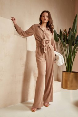 Beautiful brunette woman natural makeup wear fashion clothes casual dress code office style total beige blouse and pants suit, romantic date business meeting accessory bag interior stairs flowerpot. clipart