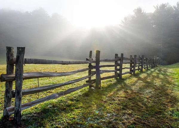 Sonnenstrahlen im nebligen Feld und gespaltener Bahnzaun — Stockfoto