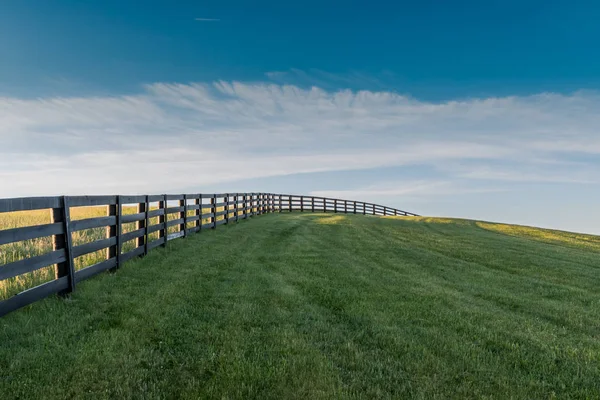 Μαύρο φράχτη οδηγεί πάνω από χορταριασμένο λόφο — Φωτογραφία Αρχείου