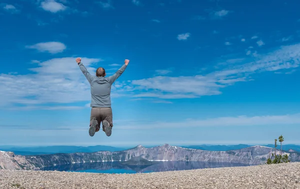 Hombre salta sobre Rocky Overlook al lago del cráter — Foto de Stock