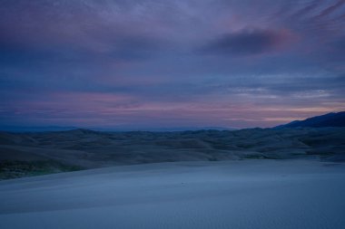 Bulutlar gün doğumunda kum tepelerinin üzerinde aydınlanmaya başlar