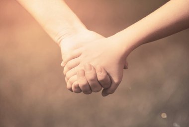 Anne, yaz günü açık havada oğlunun elini tutuyor.