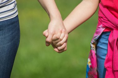 Anne, yaz günü açık havada oğlunun elini tutuyor.