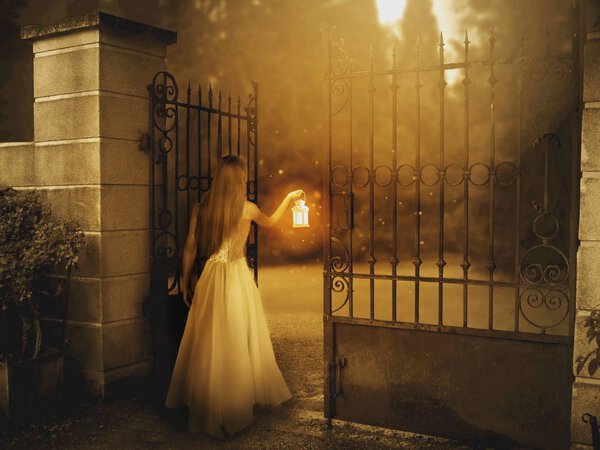 Young woman standing by the gate in sunrise with lantern