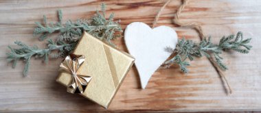 Ahşap arka planda beyaz kalpli altın bir hediye ve bitki.