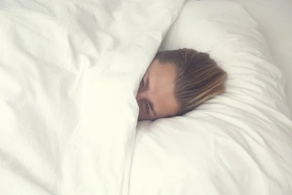 Человек, лежащий в постели и уставший смотреть на камеру — стоковое фото