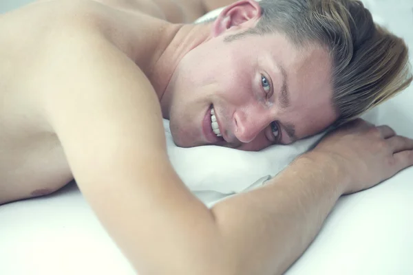 Hombre rubio en la cama sonriendo a la cámara — Foto de Stock