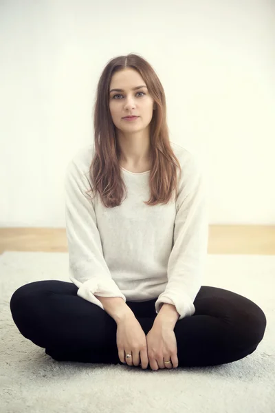 Jonge vrouw zittend op een tapijt en camera kijken — Stockfoto
