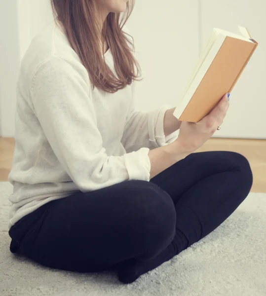 Ung kvinna sitter på golvet och läsa en bok — Stockfoto