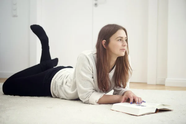 Ung kvinna liggande på golvet och läser en bok — Stockfoto