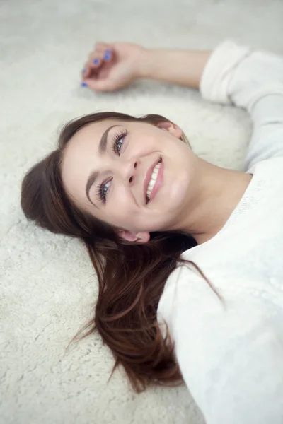Giovane donna sdraiata su tappeto e sorride — Foto Stock