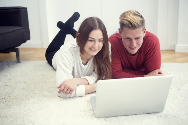 Молодая пара лежит на полу и смотрит на компьютер — стоковое фото