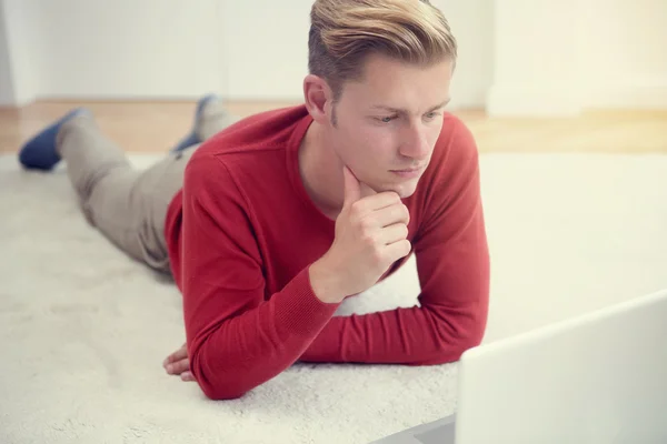 Mladý muž ležel na podlaze a při pohledu na notebook — Stock fotografie