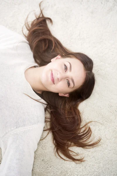 Giovane donna sdraiata sul tappeto e sorridente alla macchina fotografica — Foto Stock