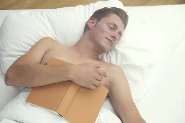 Hombre rubio durmiendo en la cama y sosteniendo un libro —  Fotos de Stock