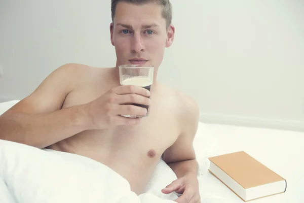 Blonder Mann liegt mit Kaffee und Buch im Bett — Stockfoto