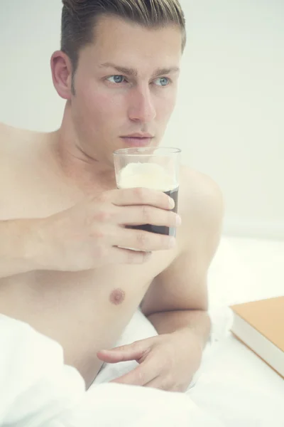 Blonder Mann liegt mit Kaffee und Buch im Bett — Stockfoto