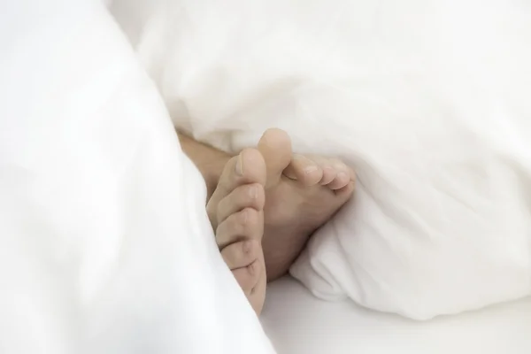 Closeup of bare feet in white bedsheets — Stock fotografie