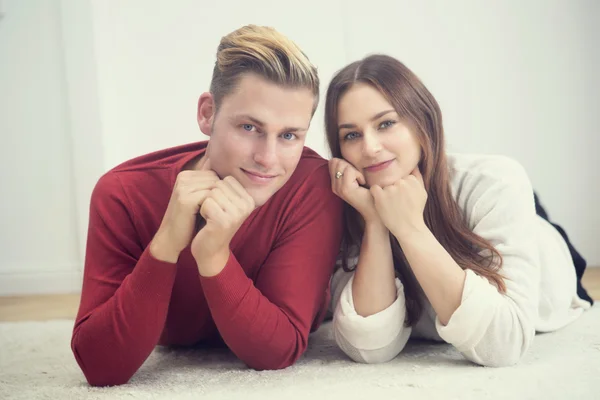 Jeune couple couché sur le tapis et souriant à la caméra — Photo