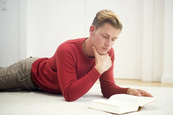 Blonde man liggen op tapijt en lezen van een boek — Stockfoto