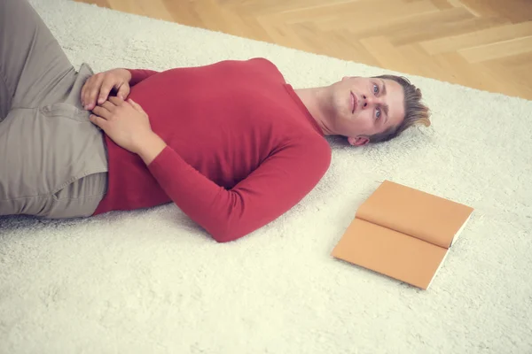 Blonde man, liggend op een tapijt met een boek — Stockfoto
