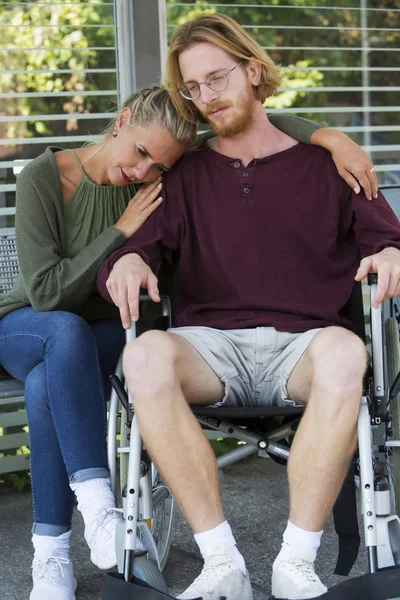 Mujer abrazando hombre en silla de ruedas y mirando triste — Foto de Stock