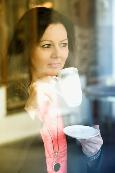 Mulher morena em pé à janela e beber café — Fotografia de Stock