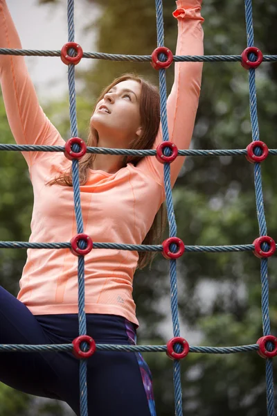 Young sporty woman climbing up a net — Stock Photo, Image