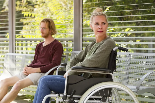 Mujer en silla de ruedas junto a un joven en el banco — Foto de Stock