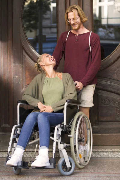 Kvinne i rullestol foran inngangen med venn – stockfoto
