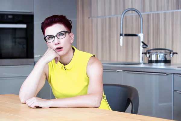 Женщина сидит за кухонным столом выглядит расстроенной — стоковое фото