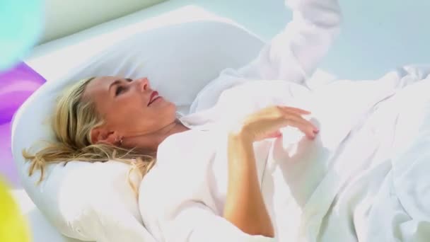 Ξανθιά γυναίκα ξαπλωμένη στο κρεβάτι και να παίζει με τα πολύχρωμα μπαλόνια — Αρχείο Βίντεο