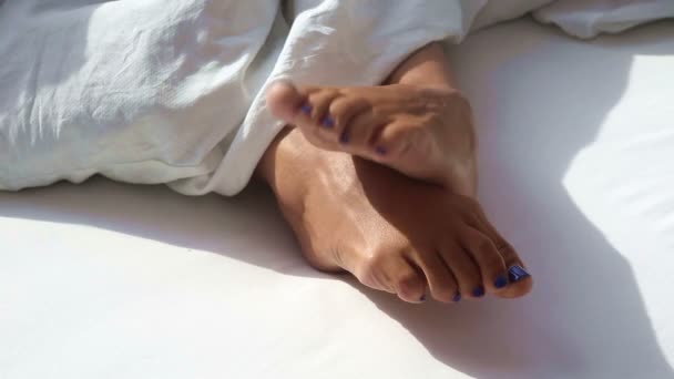 Primer plano de los pies desnudos de la mujer en la cama blanca en una mañana soleada — Vídeos de Stock