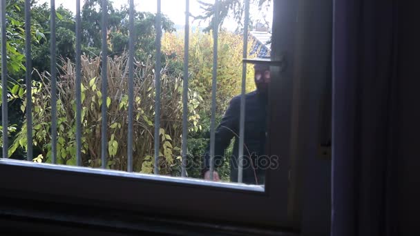 Hırsız demir çubukları olan bir pencere almaya çalışırken maskesi — Stok video