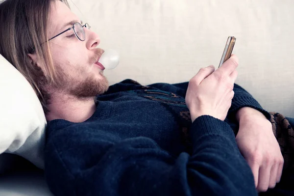 ソファ テキスト メッセージの携帯電話上で横になっている冴えない男 — ストック写真